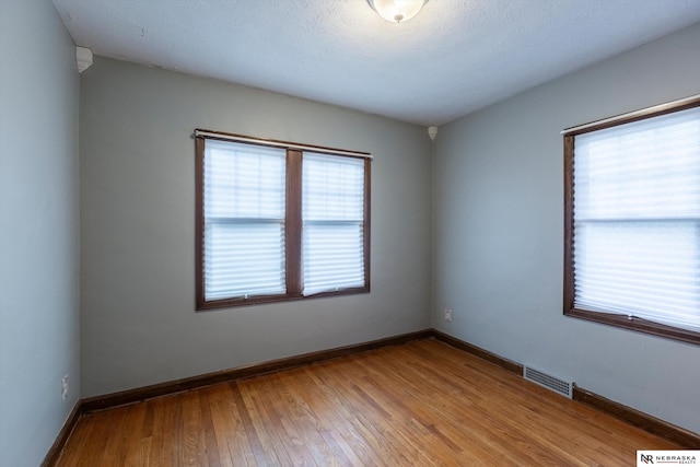 spare room with plenty of natural light, a textured ceiling, and light hardwood / wood-style flooring