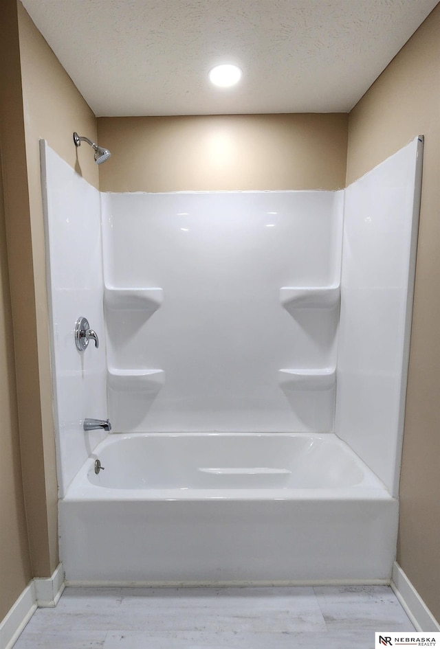 bathroom with bathing tub / shower combination, wood-type flooring, and a textured ceiling