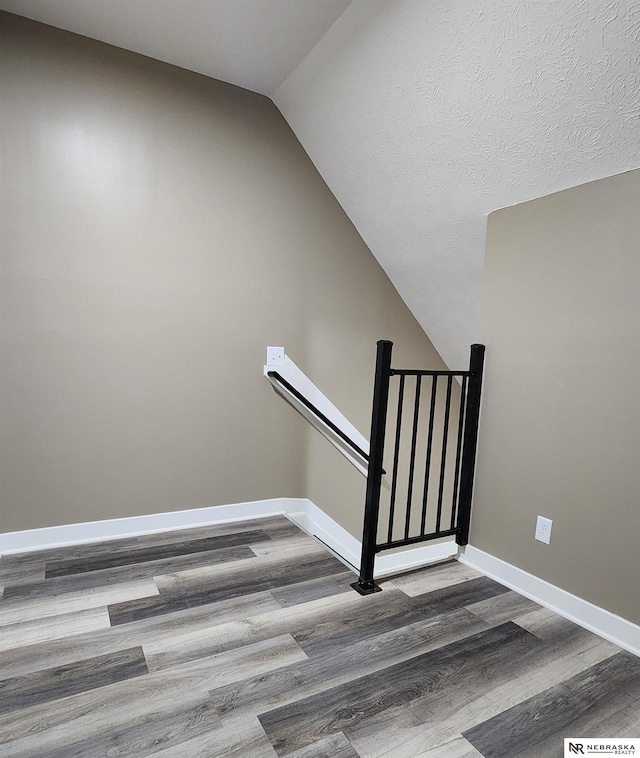 staircase with wood-type flooring, a textured ceiling, and vaulted ceiling