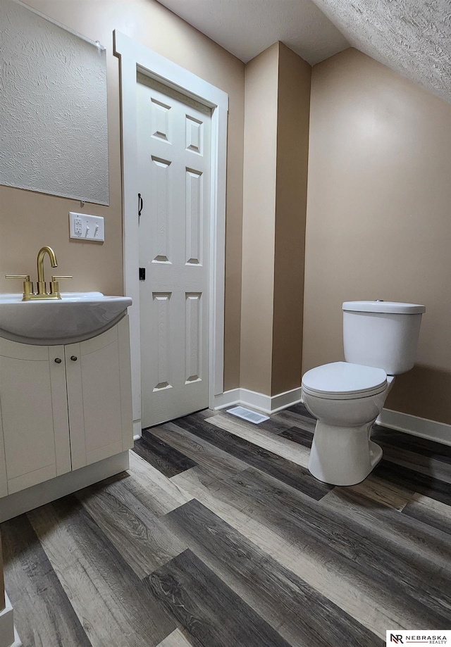 bathroom featuring vanity, vaulted ceiling, toilet, a textured ceiling, and wood-type flooring