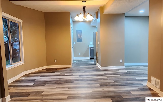 unfurnished dining area featuring a chandelier, electric panel, and hardwood / wood-style flooring