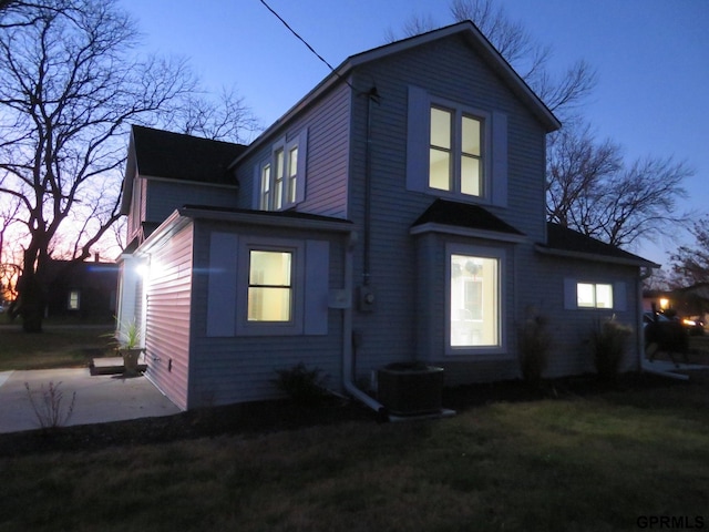 back house at dusk featuring a lawn and a patio