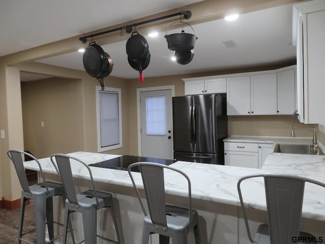 kitchen featuring light stone counters, white cabinetry, sink, and stainless steel refrigerator