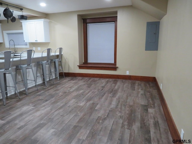 kitchen with sink, a kitchen breakfast bar, electric panel, white cabinets, and hardwood / wood-style flooring