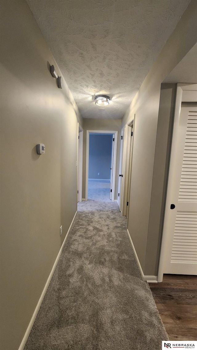 hallway featuring dark colored carpet and a textured ceiling