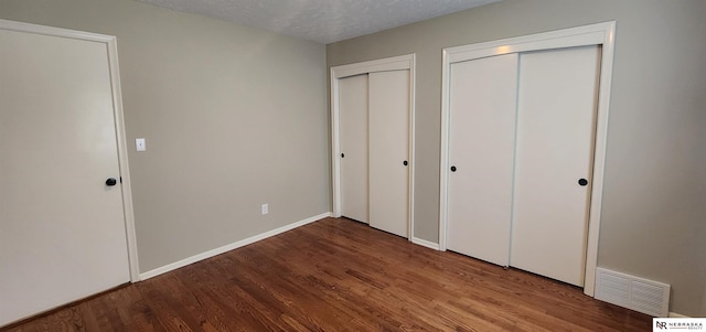 unfurnished bedroom with two closets, a textured ceiling, and hardwood / wood-style flooring