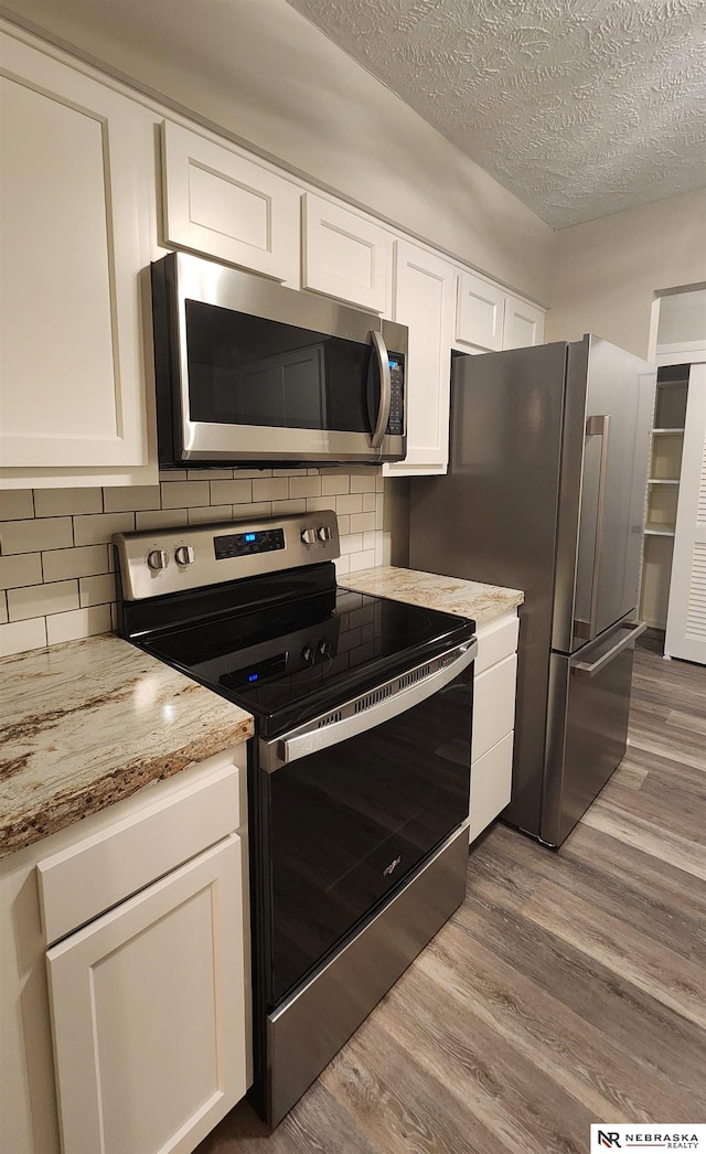 kitchen with light hardwood / wood-style flooring, a textured ceiling, light stone counters, white cabinetry, and stainless steel appliances