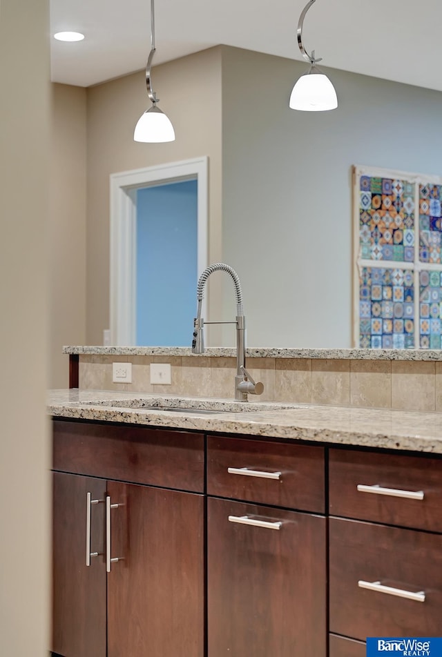 kitchen featuring pendant lighting, dark brown cabinets, light stone counters, and sink