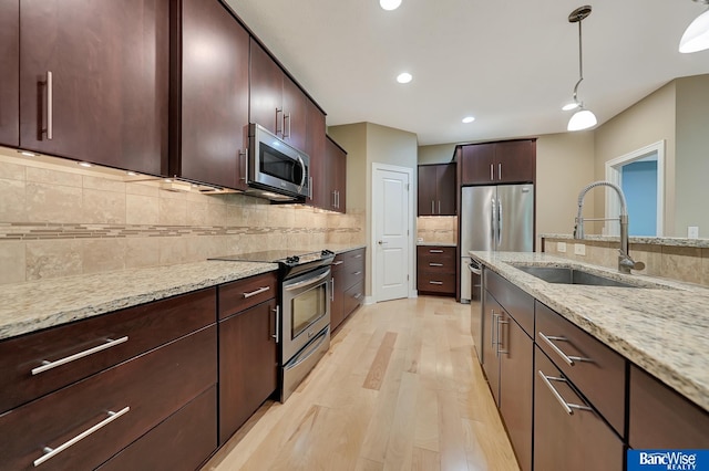 kitchen with sink, hanging light fixtures, stainless steel appliances, light stone counters, and light hardwood / wood-style floors