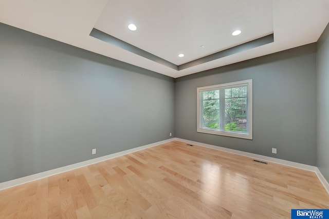 unfurnished room with a raised ceiling and light hardwood / wood-style flooring