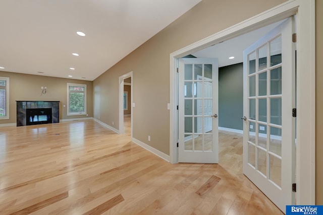 unfurnished living room with a premium fireplace, light wood-type flooring, and french doors