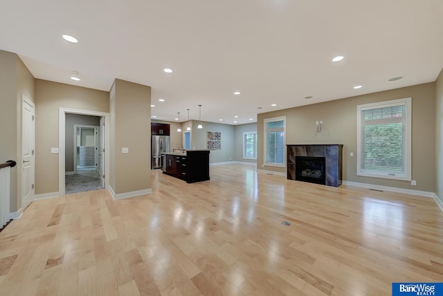 unfurnished living room with a tiled fireplace, a wealth of natural light, and light wood-type flooring