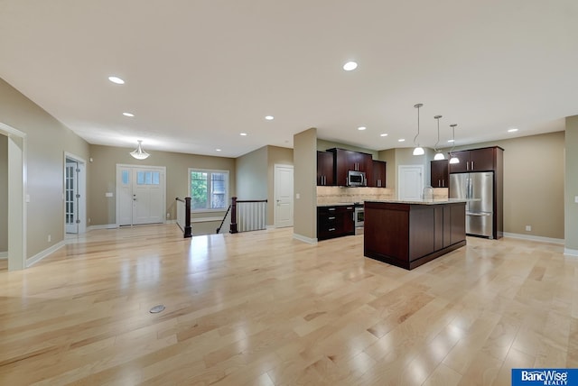 kitchen featuring light hardwood / wood-style floors, pendant lighting, dark brown cabinets, a kitchen island, and appliances with stainless steel finishes