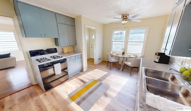 kitchen featuring ceiling fan, gas stove, sink, and light hardwood / wood-style flooring