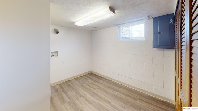 basement featuring light hardwood / wood-style floors, a textured ceiling, and electric panel