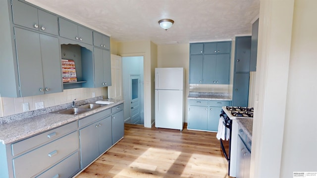 kitchen with sink, range with gas cooktop, white refrigerator, backsplash, and light hardwood / wood-style floors