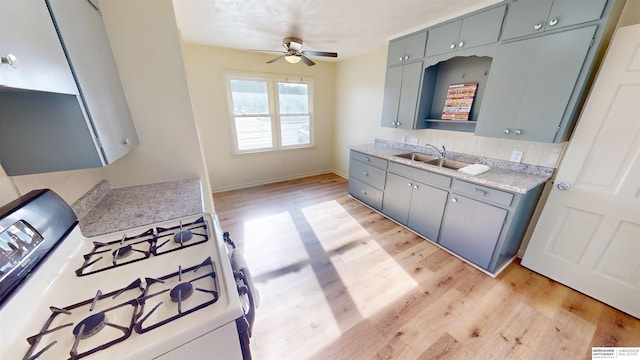 kitchen with decorative backsplash, gas range gas stove, ceiling fan, sink, and light hardwood / wood-style flooring