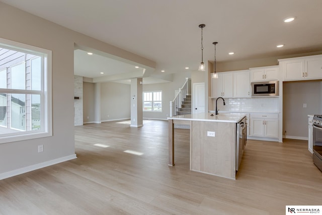 kitchen featuring a center island with sink, white cabinetry, stainless steel appliances, and hanging light fixtures