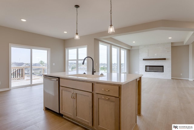 kitchen featuring sink, stainless steel dishwasher, an island with sink, light hardwood / wood-style floors, and a fireplace