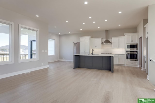 kitchen featuring white cabinets, wall chimney exhaust hood, light hardwood / wood-style floors, and appliances with stainless steel finishes