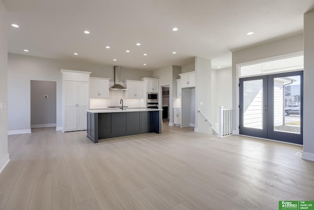 kitchen featuring white cabinetry, an island with sink, light hardwood / wood-style floors, and wall chimney range hood