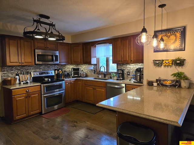 kitchen with sink, dark hardwood / wood-style floors, appliances with stainless steel finishes, decorative light fixtures, and kitchen peninsula