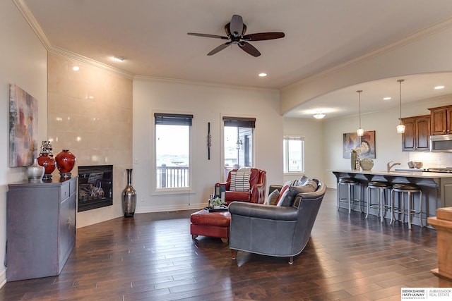 living room with a wealth of natural light, ceiling fan, dark wood-type flooring, and a tiled fireplace