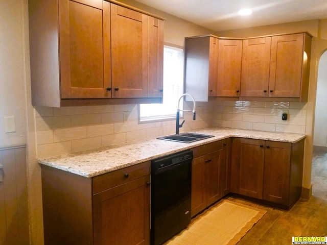 kitchen with backsplash, light stone counters, sink, black dishwasher, and light hardwood / wood-style floors