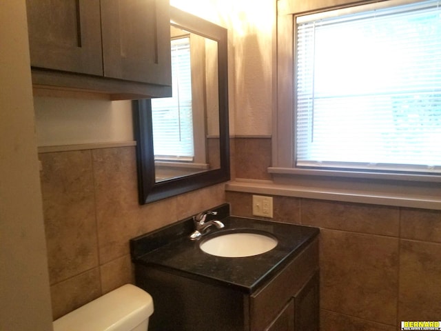 bathroom featuring plenty of natural light, toilet, tile walls, and vanity