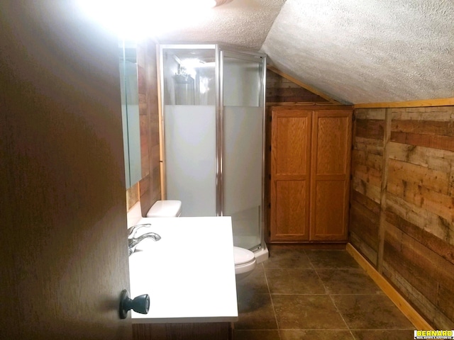 bathroom with a textured ceiling, wooden walls, lofted ceiling, toilet, and a shower with shower door