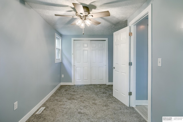 unfurnished bedroom with a textured ceiling, carpet floors, a closet, and ceiling fan