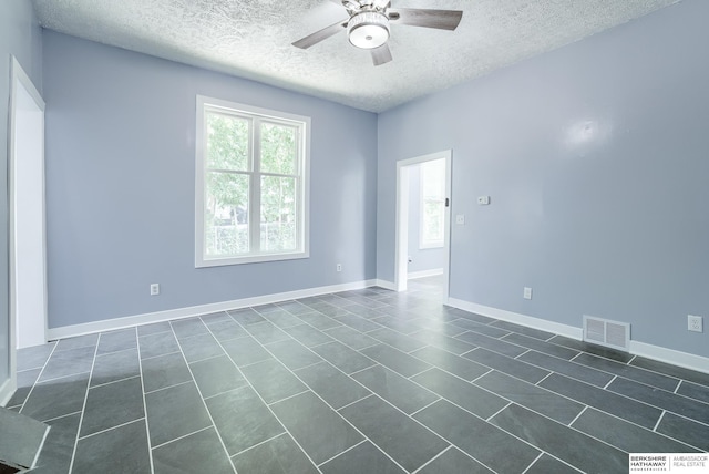 empty room with ceiling fan, dark tile patterned floors, and a textured ceiling