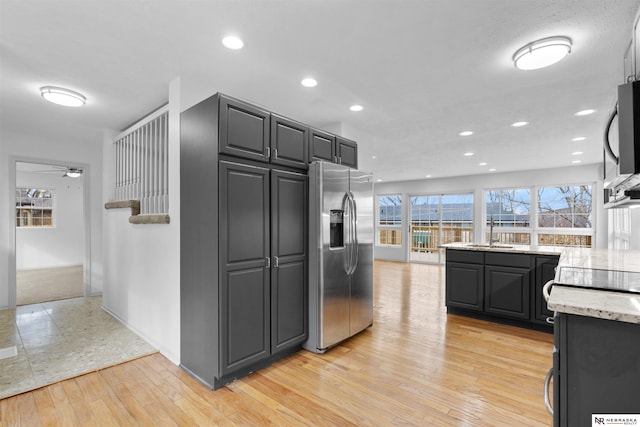 kitchen with sink, light hardwood / wood-style flooring, ceiling fan, light stone counters, and stainless steel appliances