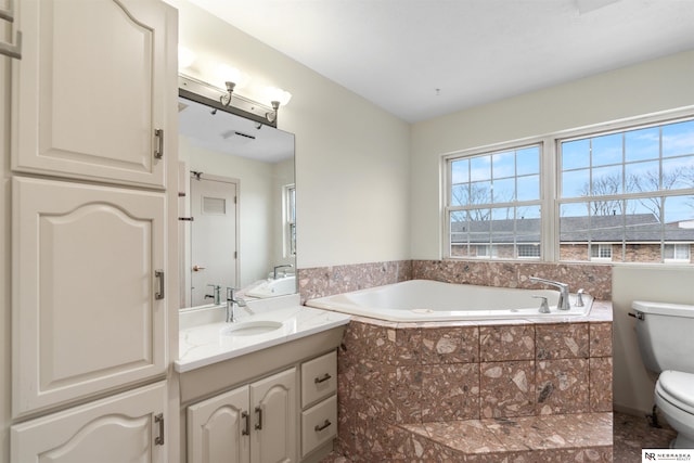 bathroom featuring vanity, tiled bath, and toilet