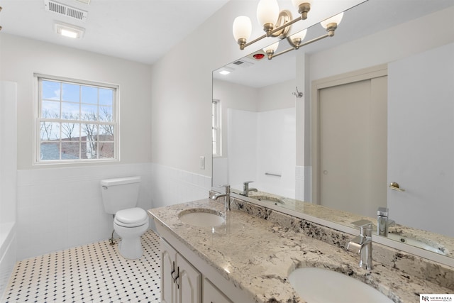 bathroom with tile patterned floors, vanity, tile walls, a chandelier, and toilet