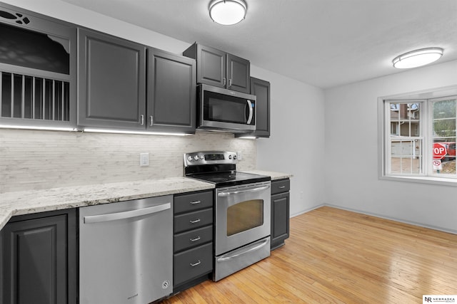 kitchen featuring light stone counters, light wood-type flooring, backsplash, and appliances with stainless steel finishes