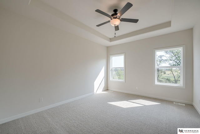 spare room with carpet, visible vents, baseboards, and a raised ceiling