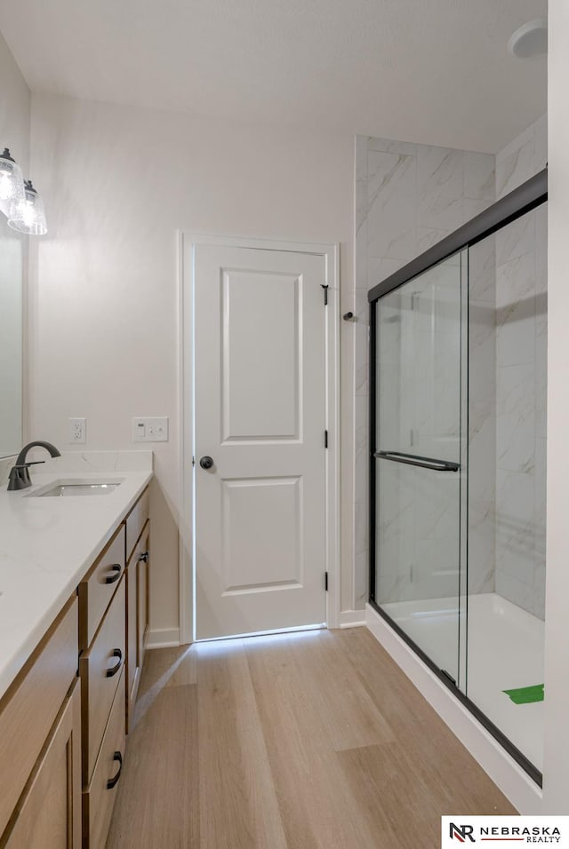 bathroom with a marble finish shower, baseboards, wood finished floors, and vanity