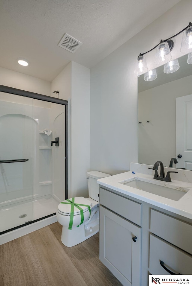 full bathroom featuring visible vents, toilet, vanity, a shower stall, and wood finished floors