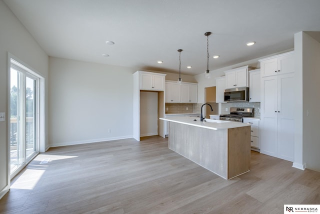 kitchen featuring light wood finished floors, light countertops, backsplash, appliances with stainless steel finishes, and an island with sink