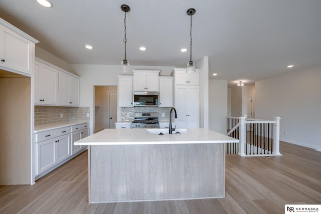 kitchen featuring an island with sink, stainless steel appliances, light wood-type flooring, white cabinetry, and a sink