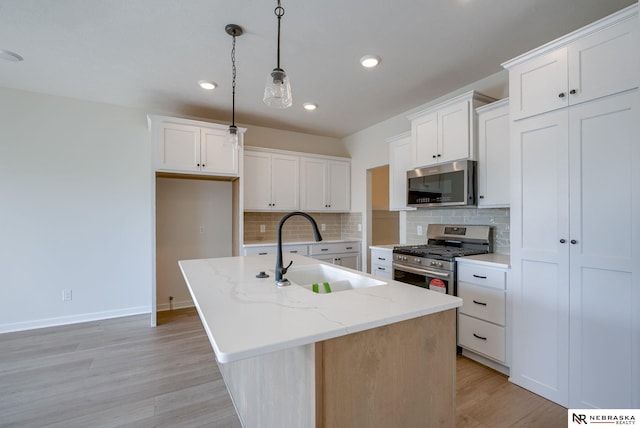 kitchen featuring light wood finished floors, white cabinets, appliances with stainless steel finishes, decorative light fixtures, and a sink