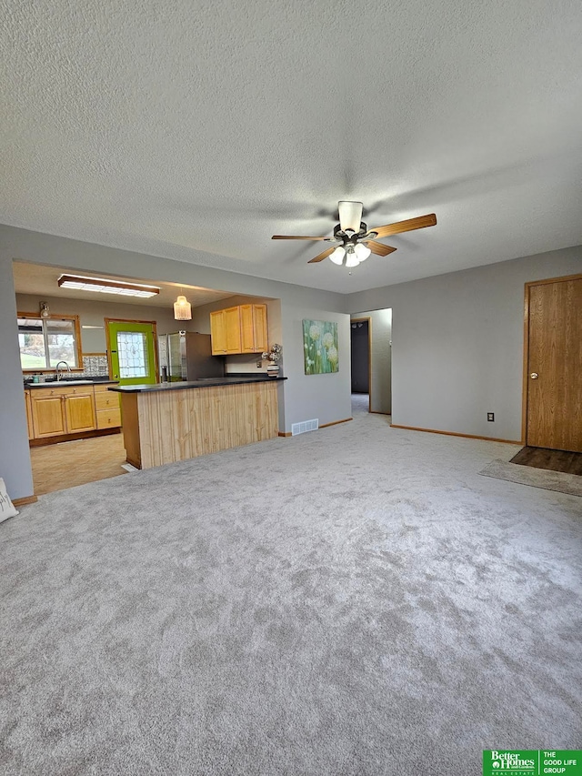 unfurnished living room with light carpet, sink, ceiling fan, and a textured ceiling