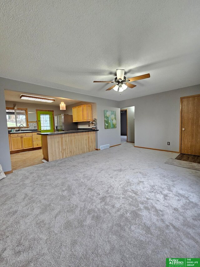 unfurnished living room featuring a textured ceiling, ceiling fan, light colored carpet, and sink