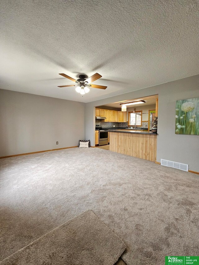 unfurnished living room with carpet, ceiling fan, and a textured ceiling