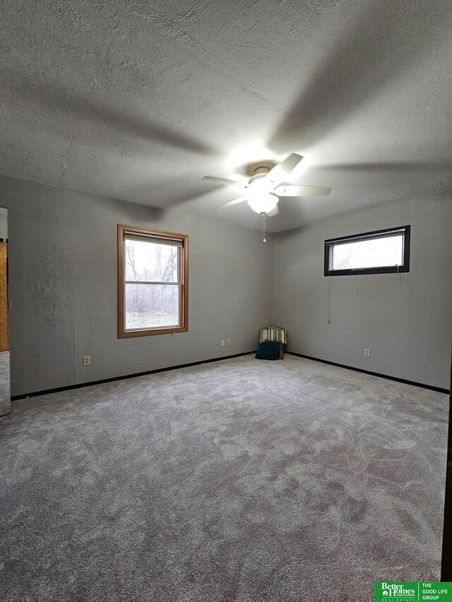 empty room with carpet flooring, ceiling fan, a textured ceiling, and a wealth of natural light