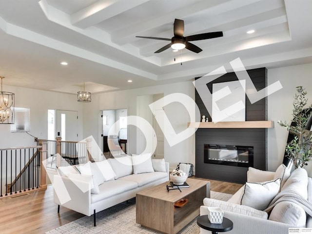 living room featuring ceiling fan with notable chandelier, light hardwood / wood-style floors, and a tray ceiling