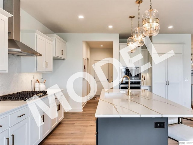 kitchen featuring pendant lighting, white cabinets, wall chimney range hood, an island with sink, and appliances with stainless steel finishes