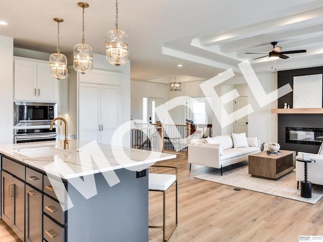 kitchen featuring stainless steel appliances, ceiling fan, pendant lighting, a center island with sink, and white cabinetry