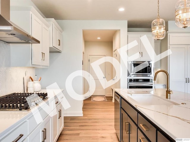 kitchen with pendant lighting, white cabinets, wall chimney range hood, sink, and appliances with stainless steel finishes